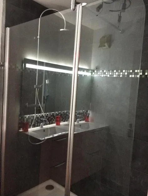 Salle de bain rénovée avec double vasque, miroir éclairé et paroi de douche